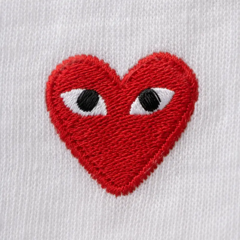 CDG Play red heart embroidery macro close-up with irregular almond eyes on white cotton