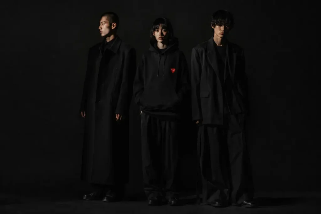 Three models in Comme des Garcons all-black layered outfits with red heart logo